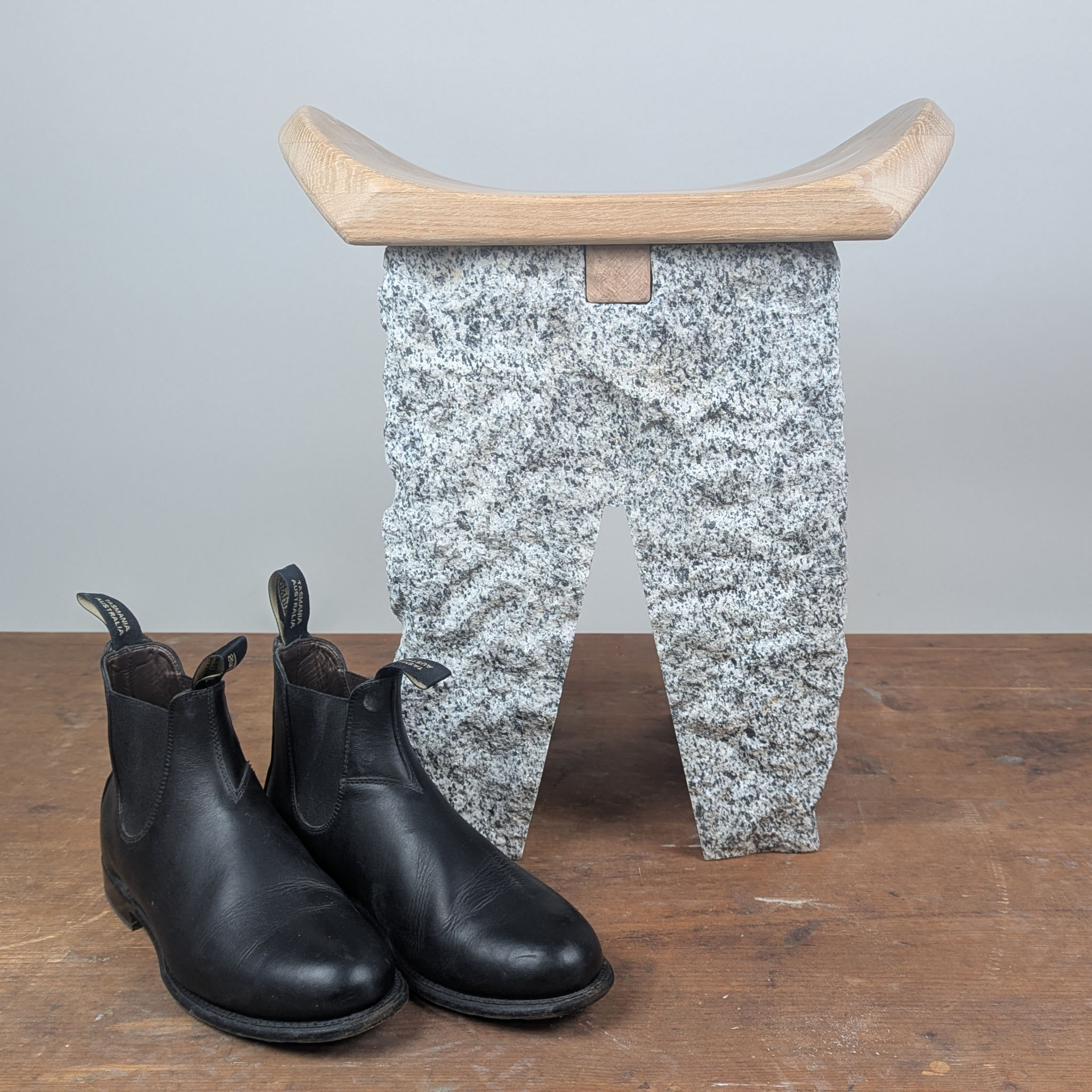 Full view of the Block Base featuring a curved oak top and granite pedestal, styled as an entryway bench with a pair of boots.