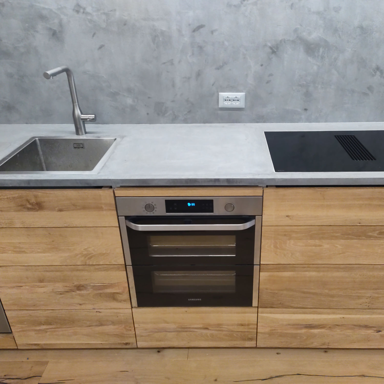 Cucina minimalista con piano in cemento, lavello integrato e frontali dei mobili in rovere naturale.