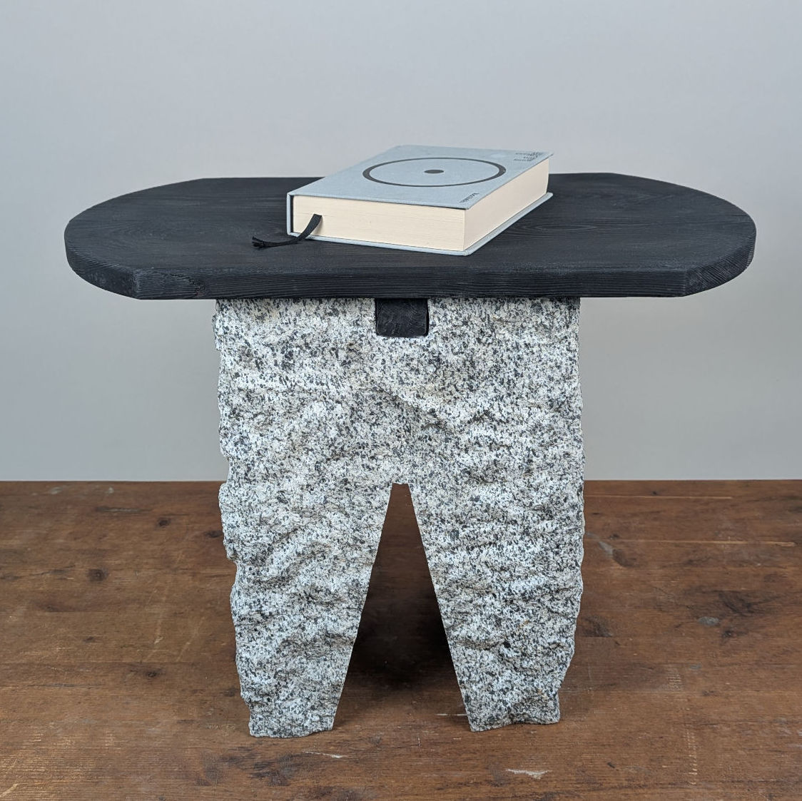 Total view of the Block Base table featuring a flat charred larch tabletop resting on a solid, sculptural granite pedestal.